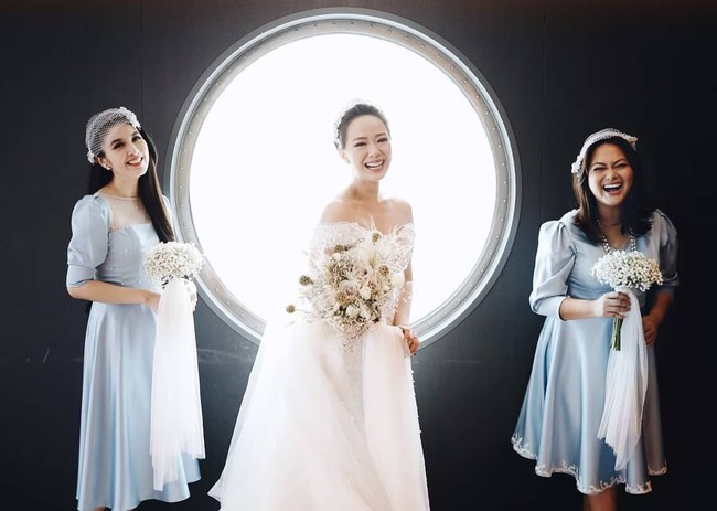 Berpose dengan latar belakang jendela khas kapal pesiar, Yuanita Christiani tersenyum bahagia diapit dua sahabat yang menjadi pengiring pengantinnya. Salah satu pengiring pengantin itu adalah artis Sandra Dewi yang terlihat semakin cantik dalam balutan dress berwarna biru rancangan Petite And The Buns. Foto: Axioo/Instagram @yuanitachrist