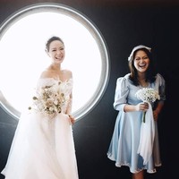 Berpose dengan latar belakang jendela khas kapal pesiar, Yuanita Christiani tersenyum bahagia diapit dua sahabat yang menjadi pengiring pengantinnya. Salah satu pengiring pengantin itu adalah artis Sandra Dewi yang terlihat semakin cantik dalam balutan dress berwarna biru rancangan Petite And The Buns. Foto: Axioo/Instagram @yuanitachrist