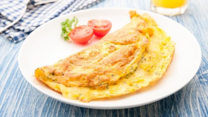 A photo of an omelette with cherry tomatoes, parsley. and grated cheese, shot from above on a rustic wooden texture with a place for text