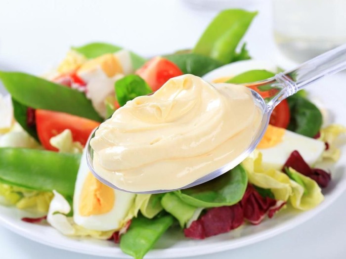 Homemade mayonnaise in bowl with eggs and spice on wooden background
