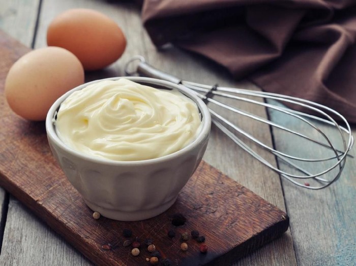 Homemade mayonnaise in bowl with eggs and spice on wooden background