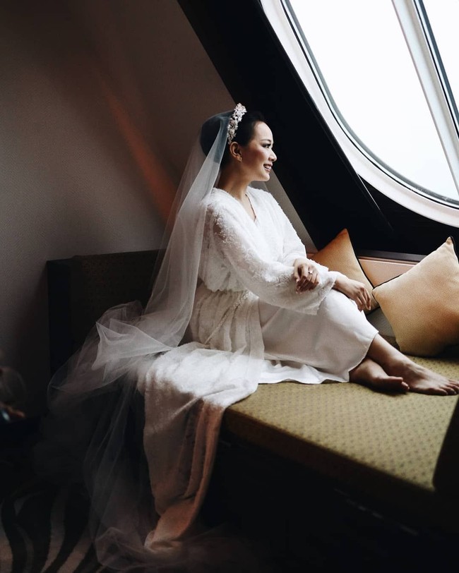 Bergaya di depan jendela kapal pesiar menjelang pemberkatan pernikahannya, Yuanita tampil cantik dan elegan dalam balutan bride robe dari Bride Kit.Foto: Axioo/Instagram @yuanitachrist