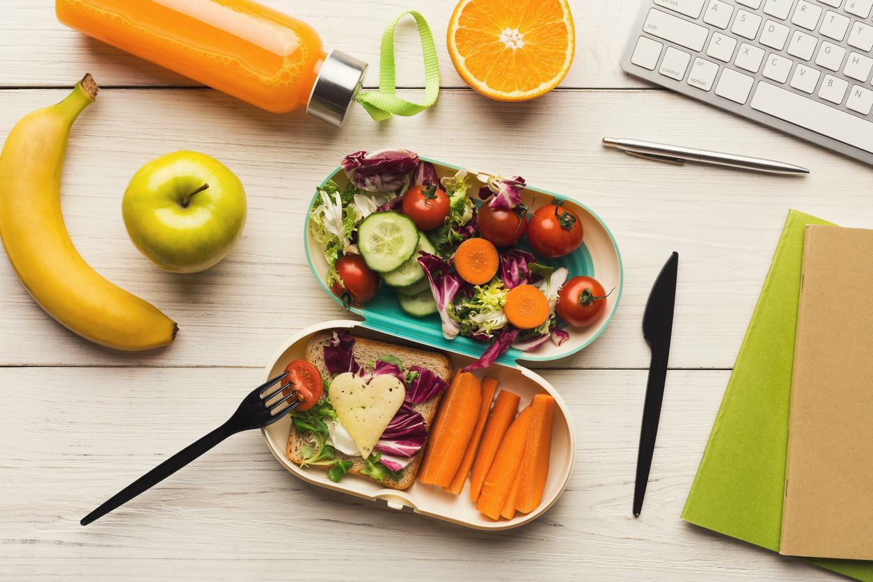 Healthy snack at office workplace. Eating organic vegan meals from take away lunch box at wooden working table with computer keyboard, top view