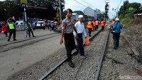 Sambil berjaga, seorang petugas polisi juga membantu warga melintas jalur KRL.
