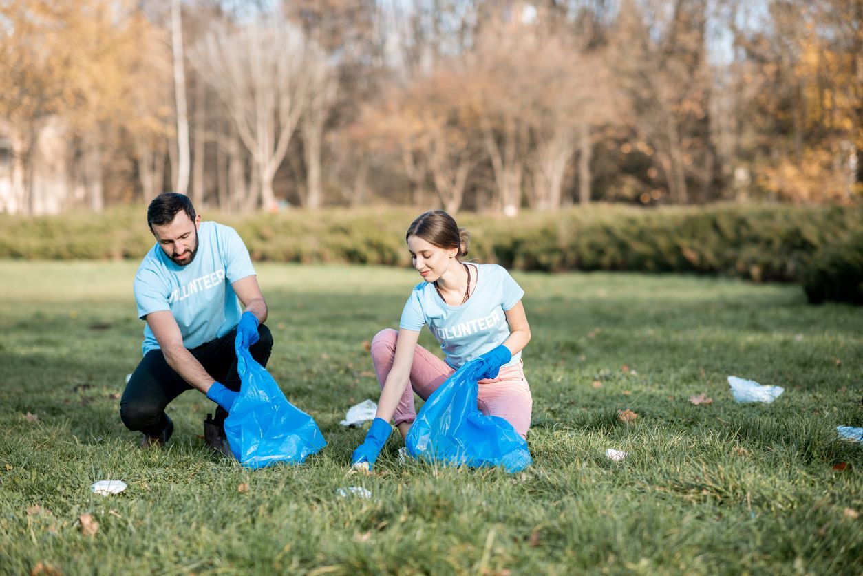 Happy man and woman volunteers dressed in blue t-shirts cleaning public garden from plastic rubbish into the bags