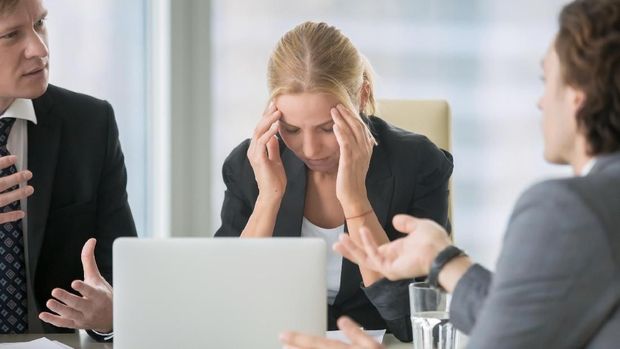 Frustrated business people sitting at the table in office, arguing while discussing project. Their female colleague covering her face with hands looking exhausted and ill. Business problem concept