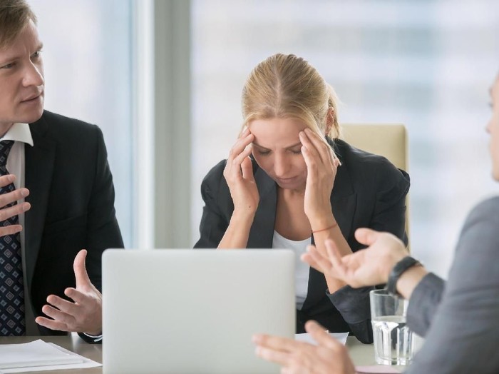 Frustrated business people sitting at the table in office, arguing while discussing project. Their female colleague covering her face with hands looking exhausted and ill. Business problem concept