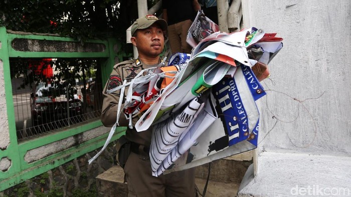 Petugas Satpol PP menertibkan alat peraga kampanye yang menyalahi aturan pemasangan di Jembatan Penyeberangan Orang, Jalan Pemuda, Rawamangun, Jakarta, Rabu (13/1/2019). Puluhan alat peraga kampanye ini ditertibkan baik baliho partai, caleg maupun spanduk pilpres.