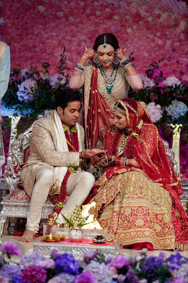 Abu Jani Sandeep Khosla merancang busana pengantin keduanya. Busana dihiasi bordiran yang dibuat secara khusus dan handmade. Mempelai wanita mengenakan lehenga paduan warna merah-emas, sementara Akash Ambani tampil mewah sekaligus elegan dalam setelan sherwani warna emas. Foto: Reliance Industries/Handout via REUTERS ATTENTION EDITORS