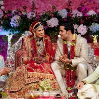 Pada hari pernikahannya dengan Akash Ambani, Shlok Mehta memakai busana tradisional India rancangan Abu Jani Sandeep Khosla. Busana dihiasi bordiran yang dibuat secara khusus dan handmade. Shlok mengenakan lehenga paduan warna merah-emas, sementara Akash Ambani tampil mewah sekaligus elegan dalam setelan sherwani warna emas. Foto: Reliance Industries/Handout via REUTERS ATTENTION EDITORS
