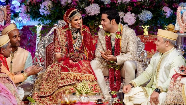 Pada hari pernikahannya dengan Akash Ambani, Shlok Mehta memakai busana tradisional India rancangan Abu Jani Sandeep Khosla. Busana dihiasi bordiran yang dibuat secara khusus dan handmade. Shlok mengenakan lehenga paduan warna merah-emas, sementara Akash Ambani tampil mewah sekaligus elegan dalam setelan sherwani warna emas. Foto: Reliance Industries/Handout via REUTERS ATTENTION EDITORS