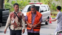 Dia datang dengan tangan diborgol dan memakai rompi tahanan.