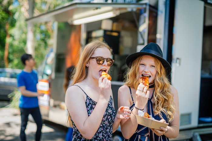 Group of young people standing in front of the food truck with delicious fast food. Diverse people buying tasty pastry, sandwiches and hamburgers in famous food truck, near the festival venue.