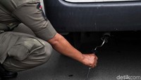 Petugas memasukan alat uji emisi ke knalpot sebuah mobil.