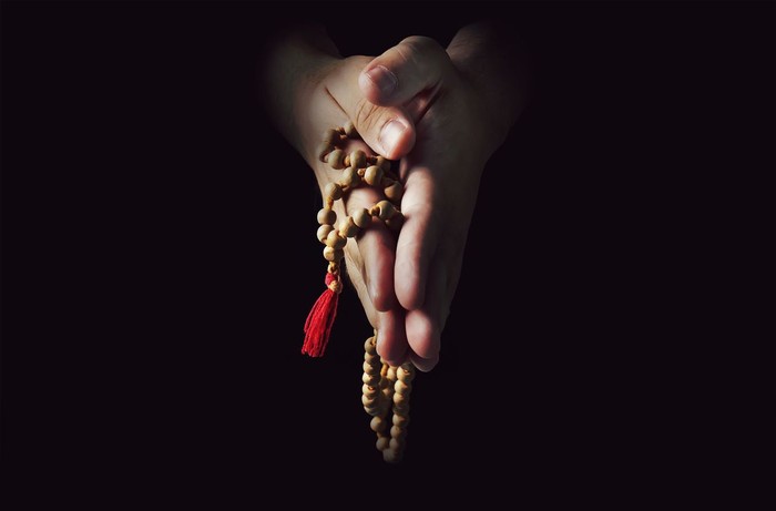 Hands folded in prayer on a black isolated background. The priest in prayer. Rosary in the hands of men