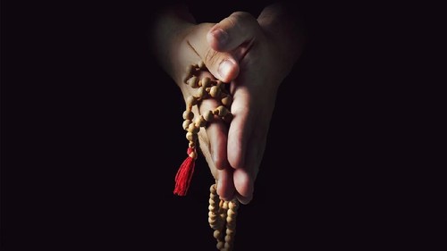 Hands folded in prayer on a black isolated background. The priest in prayer. Rosary in the hands of men