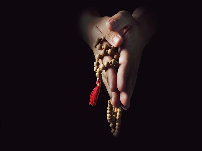 Hands folded in prayer on a black isolated background. The priest in prayer. Rosary in the hands of men