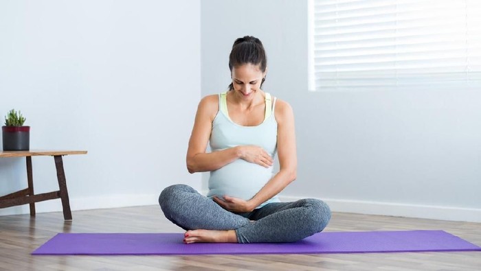 olahraga hamil Pregnancy yoga meditation. Full length healthy 8 months pregnant calm Asian woman meditating or doing yoga exercise at home. Relaxation yoga sitting side stretch positions.