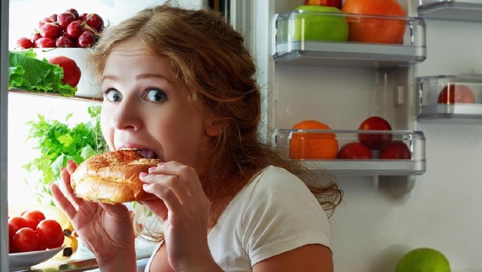 woman eats sweets at night to sneak in a refrigerator