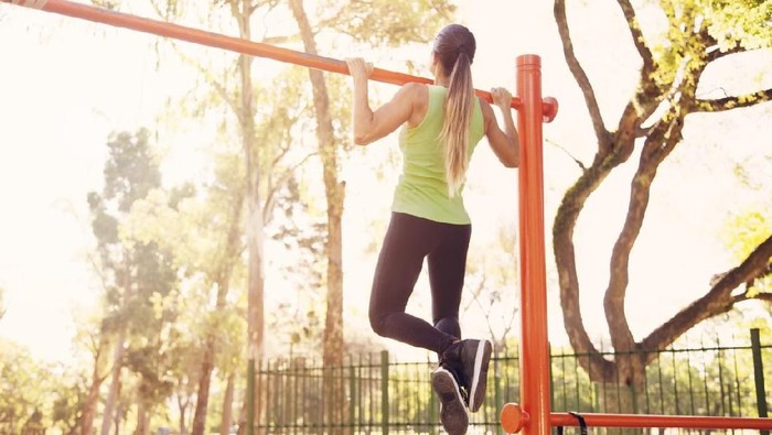 Fit woman using gymnastic rings as part of a cross training workout at the gym. Muscular young female athlete exercising with rings.