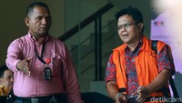 Sambil membawa tas, dia hanya diam saat menuju mobil tahanan.