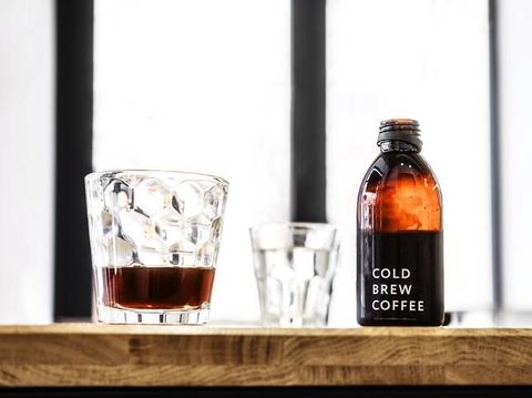 Fresh hot coffee being poured into a cup from a stainless steel french press in a trendy cafe