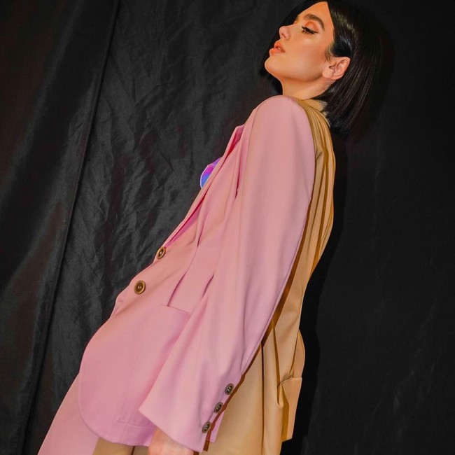 Penampilannya edgy dibalut setelan oversized berwarna pink dengan aksen two-tone coklat di bagian kerah hingga belakang jas. Foto: Instagram @dualipa