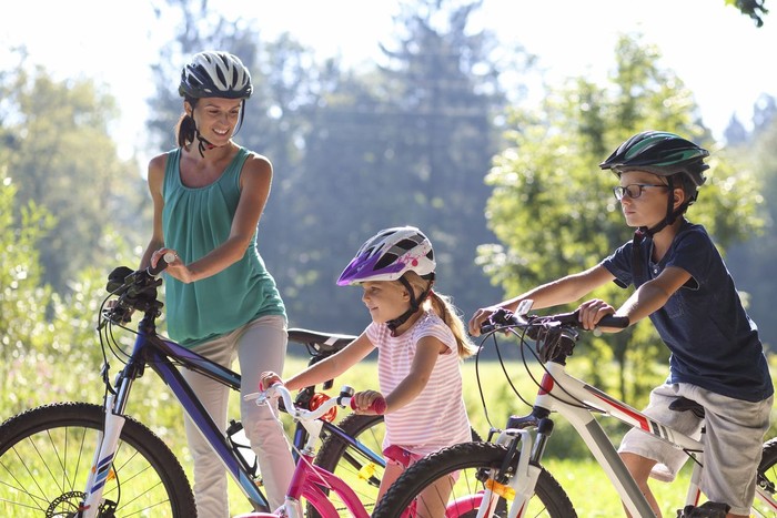 Young mother looking proud and happy at her boy and girl on a bicycle ride through the park.