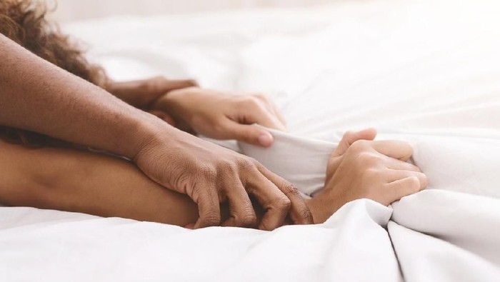 Passion in bed. African-american couple hands pulling white sheets in ecstasy, closeup