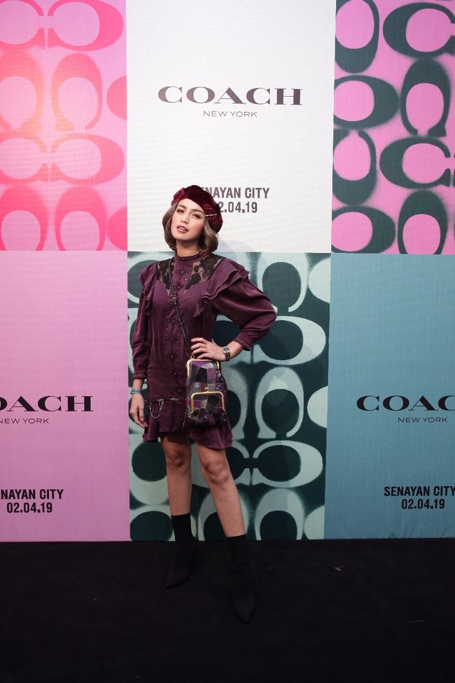 Jessica Iskandar mengandalkan tampilan yang chic dengan dress berhias ruffle marun yang senada dengan topi baret velvetnya. Tidak ketinggalan tas Coach selempang bermotif patchwork. Foto: Dok. Coach
