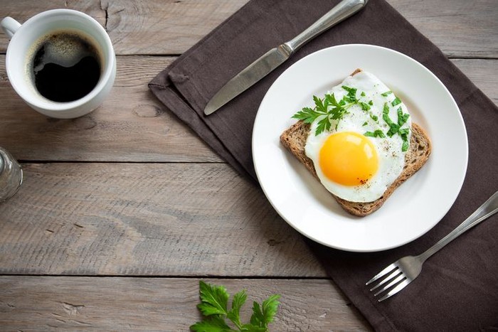 Fried Egg on Toast and cup of Coffee for Breakfast. Fried egg with bread on plate over wooden table, top view, copy space.