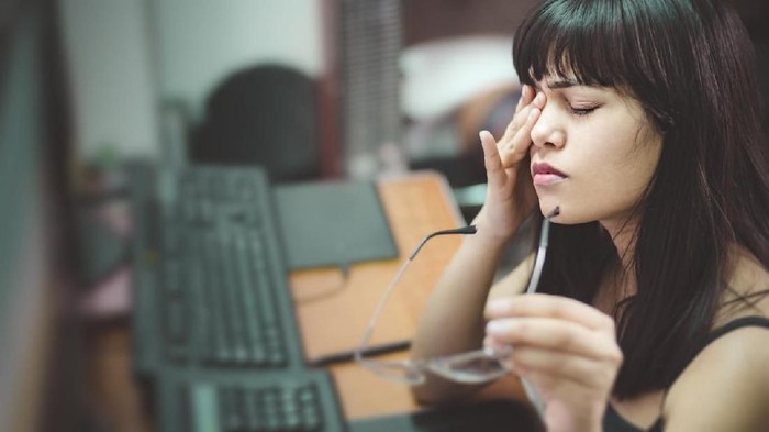 Asian, Indian young woman rubbing her eye and holding eyeglasses. She is suffering with aching eyes while working long hours on computer at home.