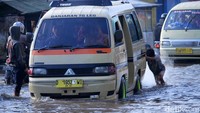 Seorang bocah mendorong angkot di tengah banjir.
