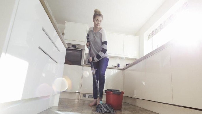One woman mopping the floor in her kitchen.