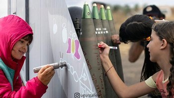 Anak perempuan yang harus meninggalkan negaranya karena perang sedang menggambar grafiti di dinding di sebuah kamp pengungsi di Yunani. Anak-anak perempuan menulis pesan di misil di unit artileri selama perang Israel-Lebanon 2006. (L) Foto: Uğur Gallenkuş