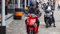 Di belakang Nasir ada beberapa orang yang mengendarai motor Gesits berwarna hitam dan putih.