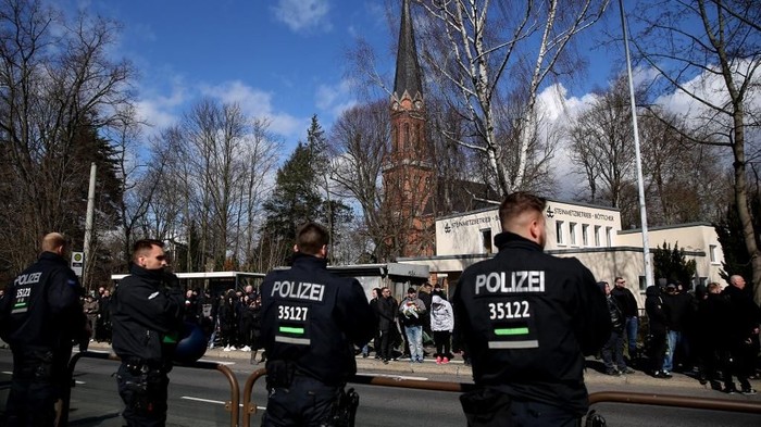 Policemen and mourners stand at the roadside, where a hearse transported the coffin of Thomas Haller, a leading figure in eastern Germanys far-right scene and fan of German fourth-tier football club Chemnitzer FC, to the cemetery in Chemnitz, eastern Germany, on March 18, 2019; in background can be seen the Michaeliskirche church. - A political storm was whipped up in Saxony state before a match on March 9, 2019 against Altglienicke when Chemnitz fans paid tribute before kick-off to Haller, who had for years provided security for the club and co-founded the HooNaRa (Hooligans-Nazis-Racists) group in the 1990s that was disbanded in 2007. (Photo by Ronny Hartmann / AFP)