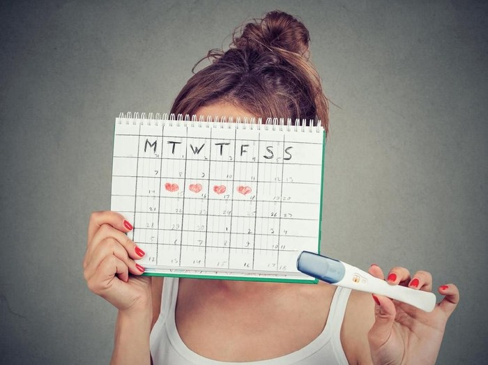 masa subur Young woman hiding behind a periods calendar and showing a positive pregnancy test
