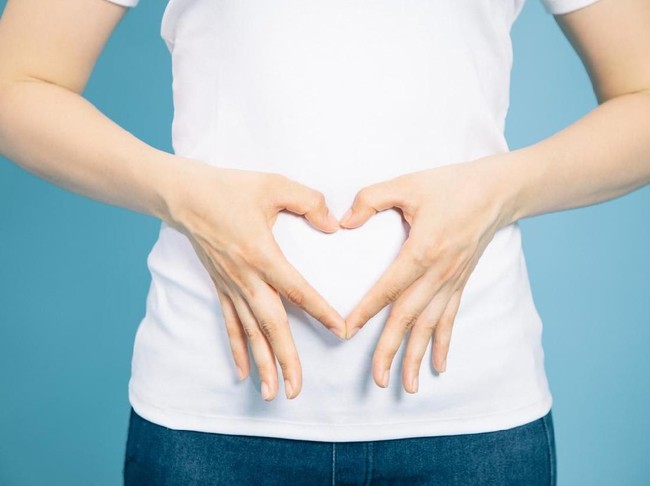 young woman who makes a heart shape by hands on her stomach.