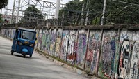 Bajaj melintas di depan dinding yang penuh dengan coretan.