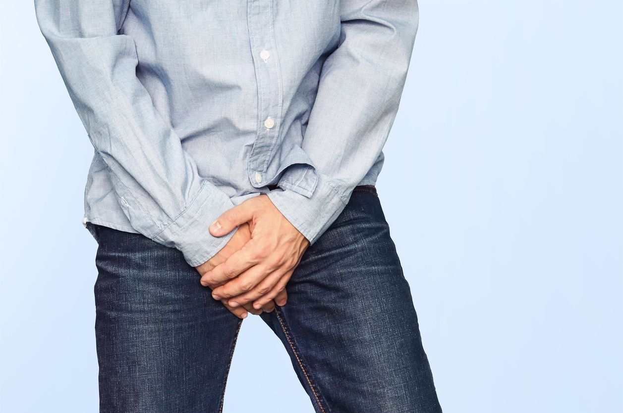 Close up of a man with hands holding his crotch on a light blue background. Urinary incontinence. Men's health. The pain from the blow in groin.