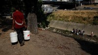 Orang-orang mengumpulkan air dari selokan yang mengalir ke Sungai Guaire, yang membawa sebagian besar air limbah kota.