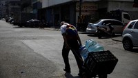 Seorang lelaki menarik gerobak sorong yang diisi dengan wadah berisi air.