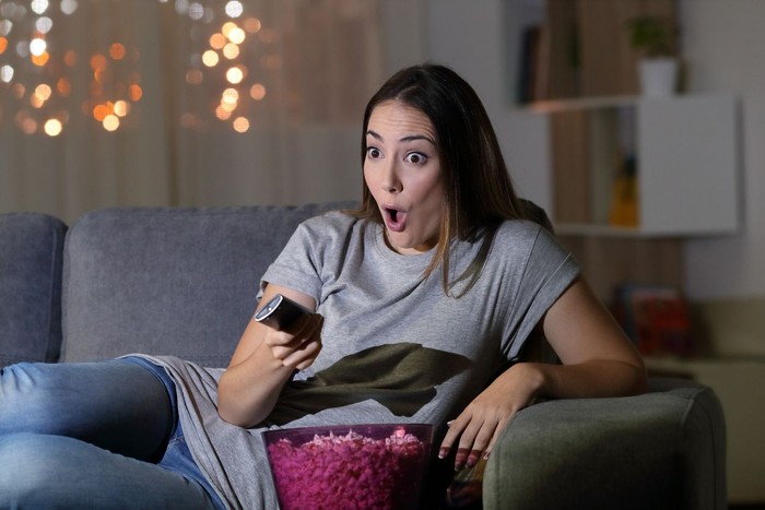 Amazed woman watching tv in the night sitting on a couch in the living room at home