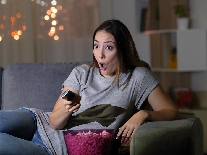 Amazed woman watching tv in the night sitting on a couch in the living room at home