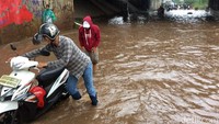 Pengendara motor menuntun motornya yang mogok akibat memaksa menerobos jalan yang terendam banjir di Jalan Kyai Haji Noer Ali, Bekasi.