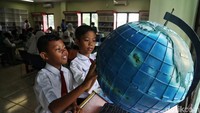 Dua orang anak tengah belajar membaca peta dunia.