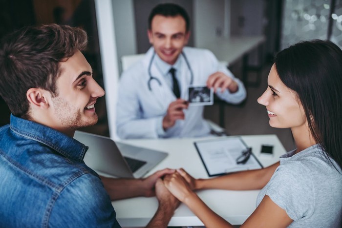 Young couple at the doctor. Holding hands and looking on each other while doctor is showing the ultrasond picture of their future baby.