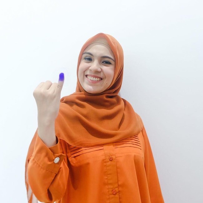 Nycta Gina memilih warna yang berbeda saat mendatangi TPS. Ia tampil memakai busana bernuansa oranye. Istri presenter Kinos ini juga memilih hijab segi empat berbahan voile yang nyaman. Foto: Instagram