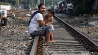 Seorang ibu menemani anaknya bermain di rel kereta api.